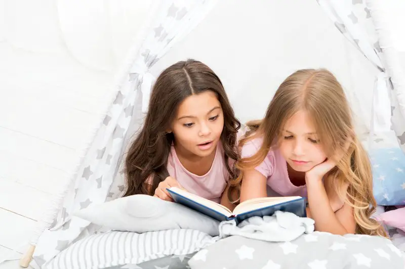 Girls best friends read fairy tale before sleep. Best books for kids. Children read book in bed. Reading before bed can help sleep better at night. Stories every kid should read. Family tradition.