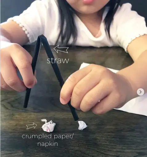 kid picking up crumpled paper using a straw